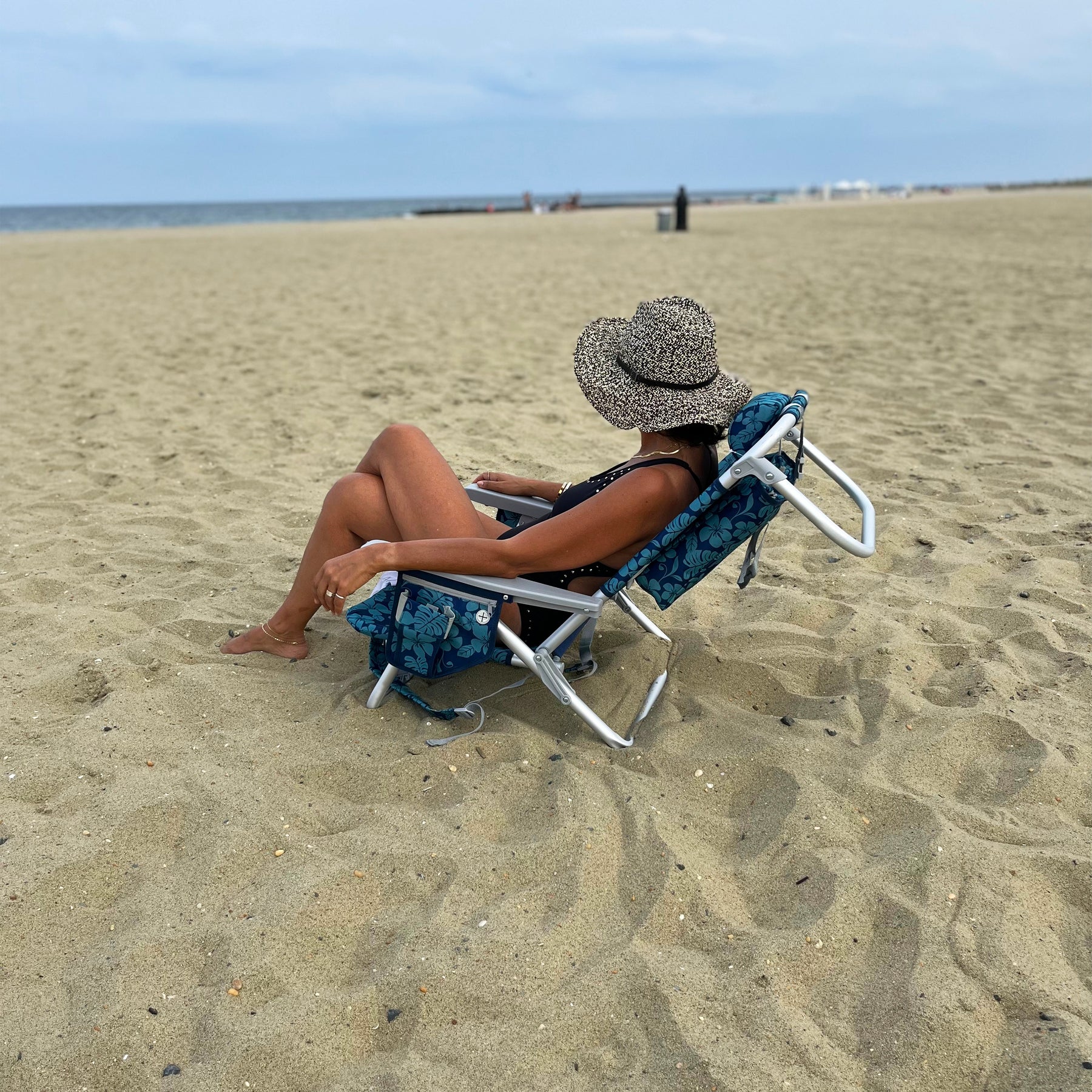 Woman relaxing on the beach in the Backpack Aluminum Blue Flower Beach Chair.