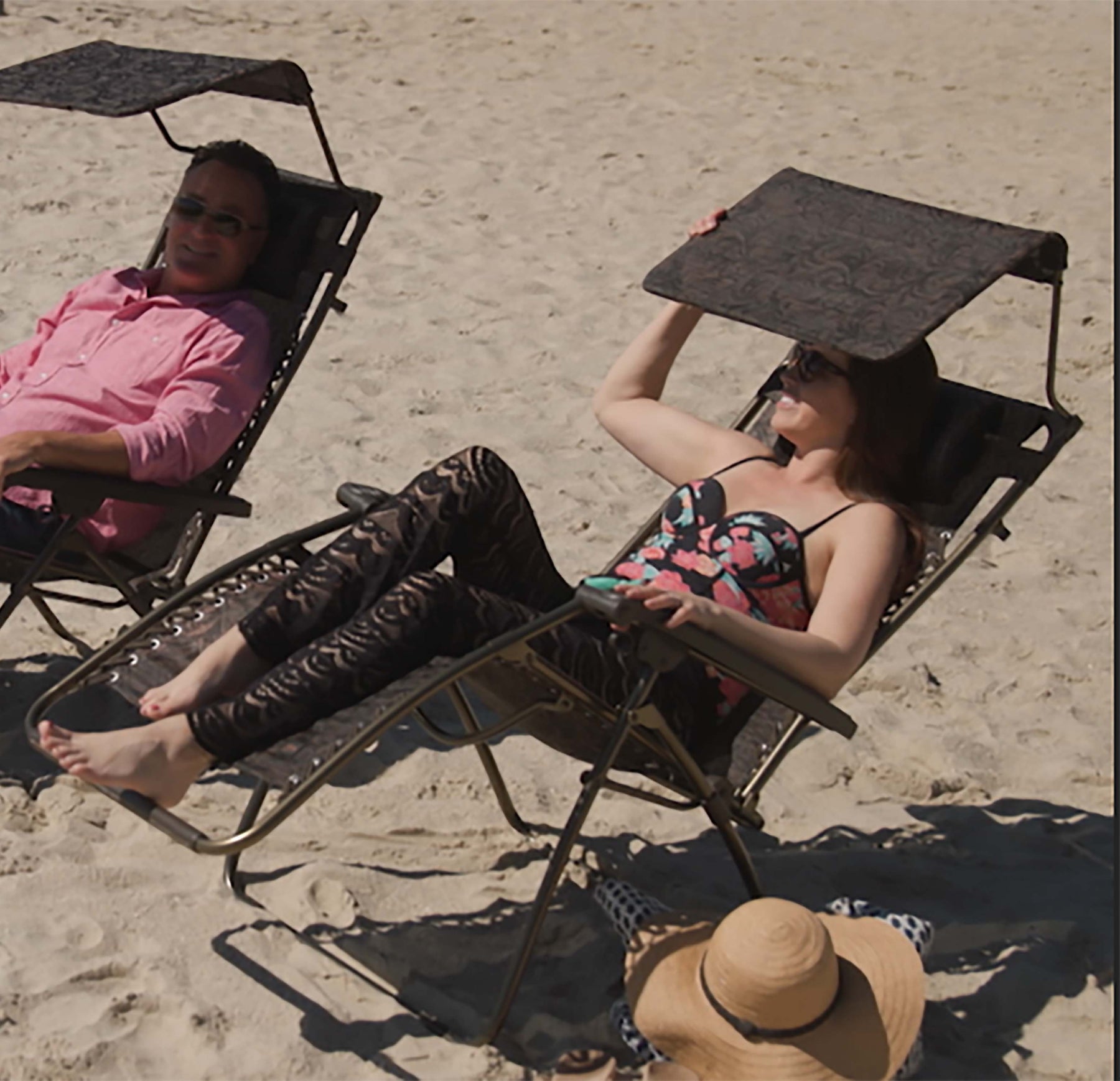 Man and woman relaxing on the beach in the Bliss Hammocks 30-inch wide Gravity free chair, using the canopy to block the sun.