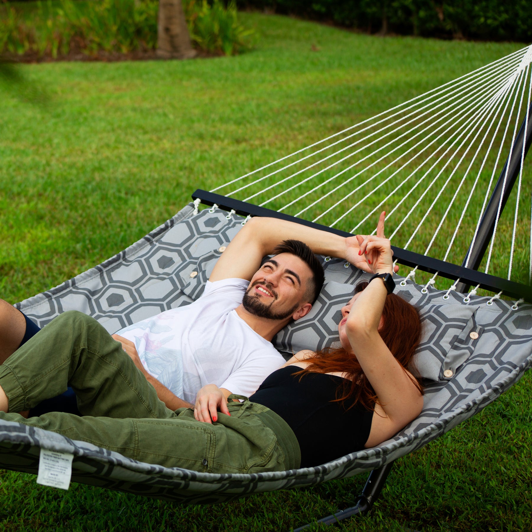 Man and woman looking up into the sky while relaxing outside in the grass on a Close up of the fabric and pattern for the Bliss Hammocks 55-inch Wide 2-Person Reversible Quilted Hammock with spreader bars and a pillow.