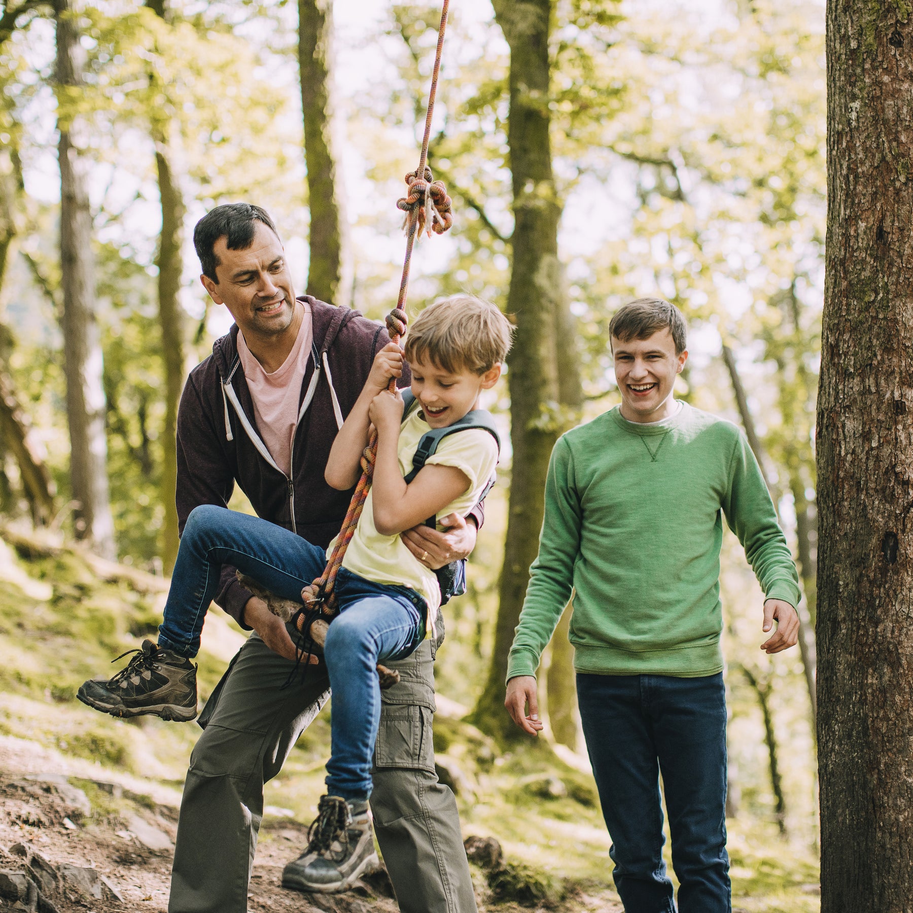 Father pushing his joyful son on the Bliss Outdoors Rope Climber Swing that is hanging from a tree outside.
