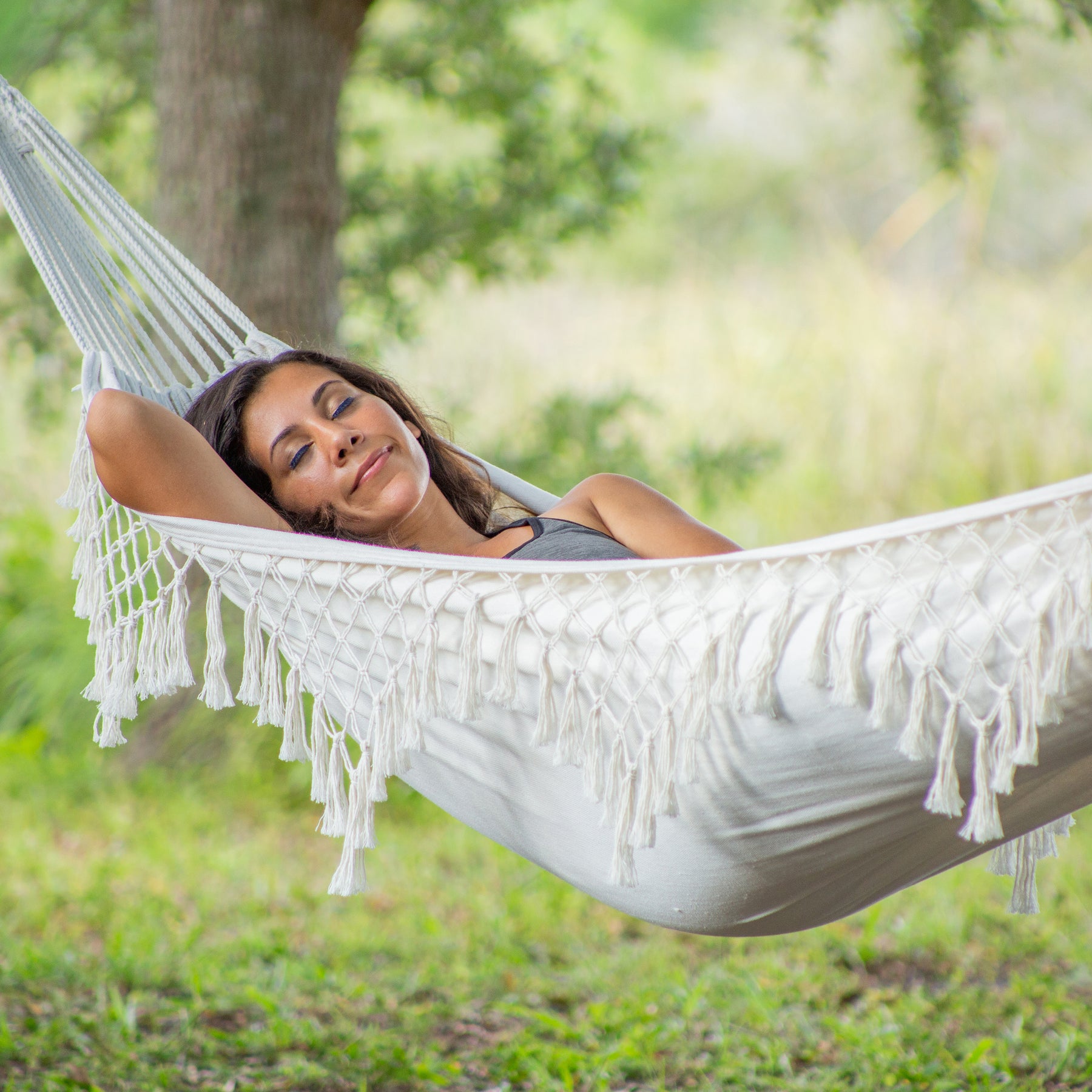 Woman relaxing in a Bliss Hammocks fringed hammock outside with nature around her.