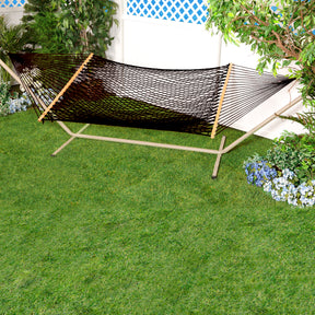 Black Variation of Bliss Hammocks 60-inch Wide Cotton Rope Hammock with a stand in a yard by some flowers and a fence.