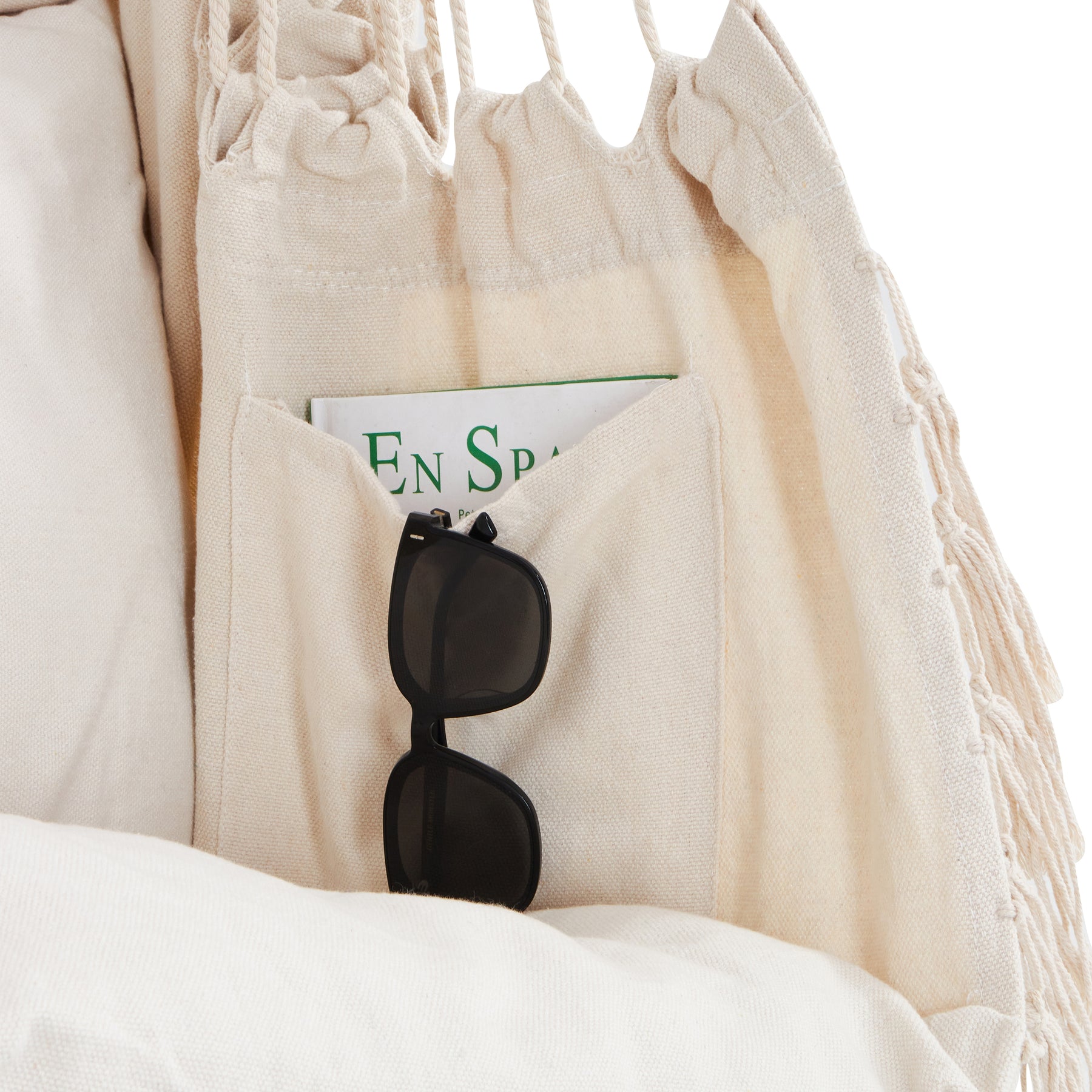 Close-up of the pocket on the inside of the Bliss Hammocks 40-inch Wide Fringed Hammock Chair in the natural variation. There's a book inside and sunglasses hanging on the pocket.