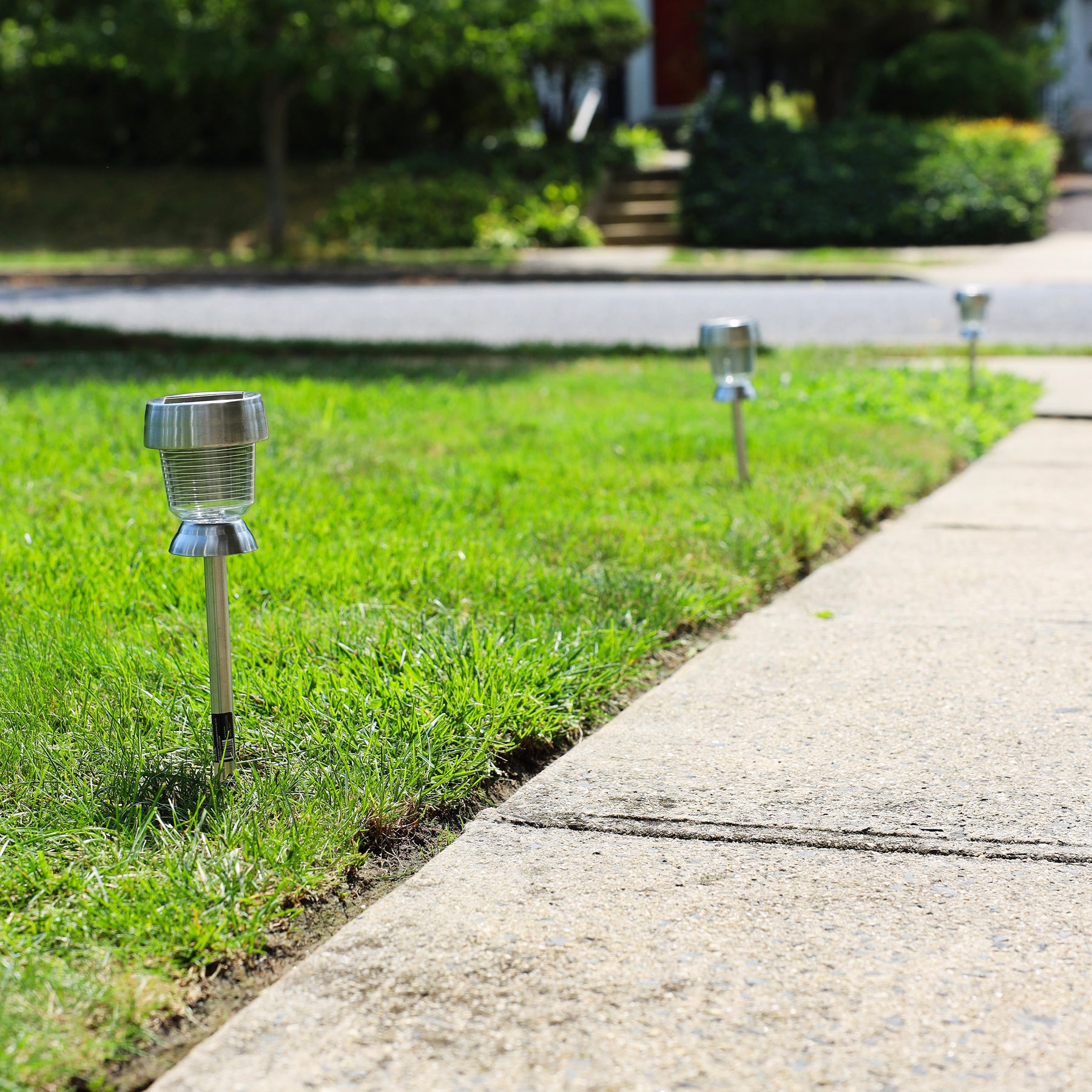 3 solar powered led lights staked in the ground along the side of a pathway.