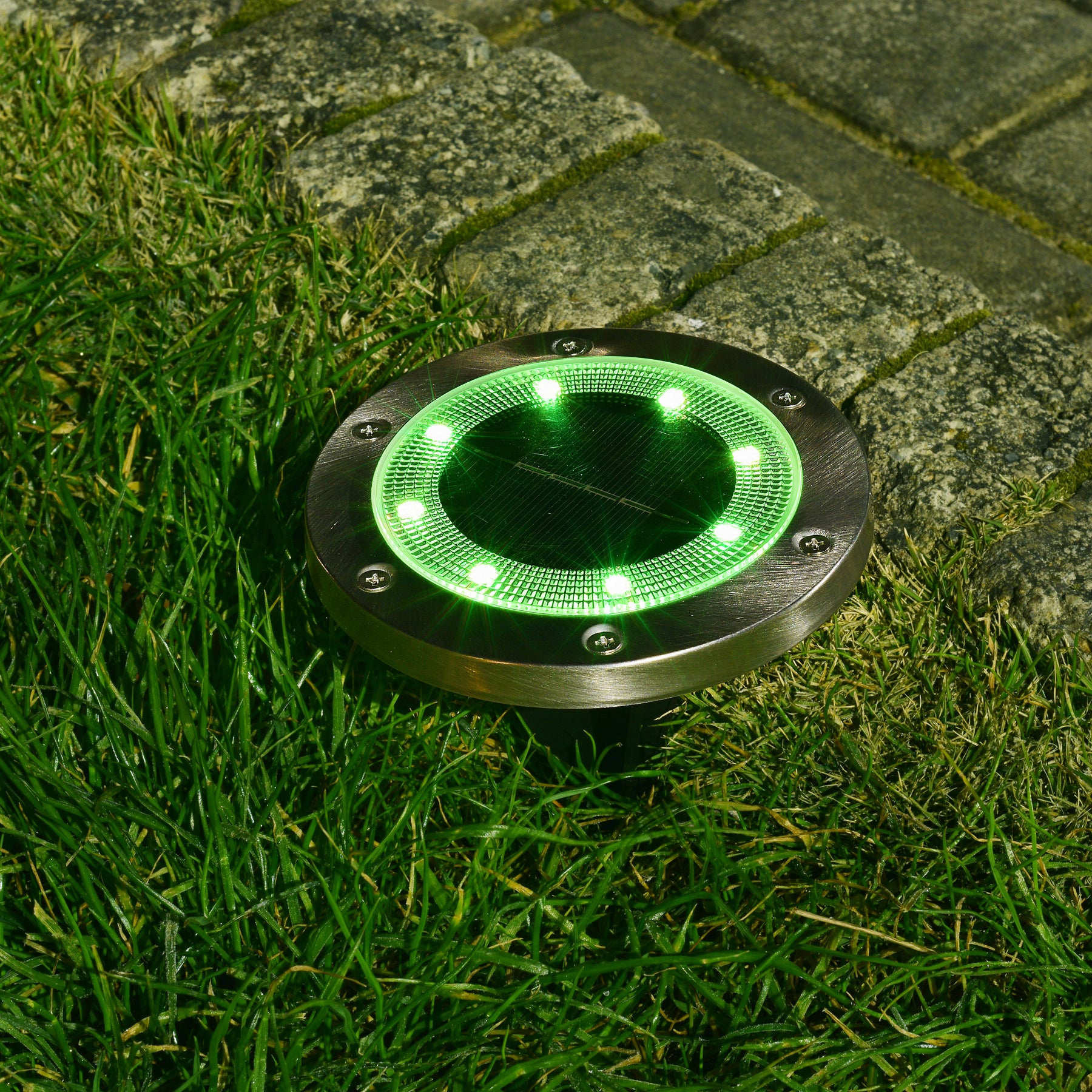 Bliss Outdoors Solar Powered LED Metal Disc Pathway light in the ground lighting up green.