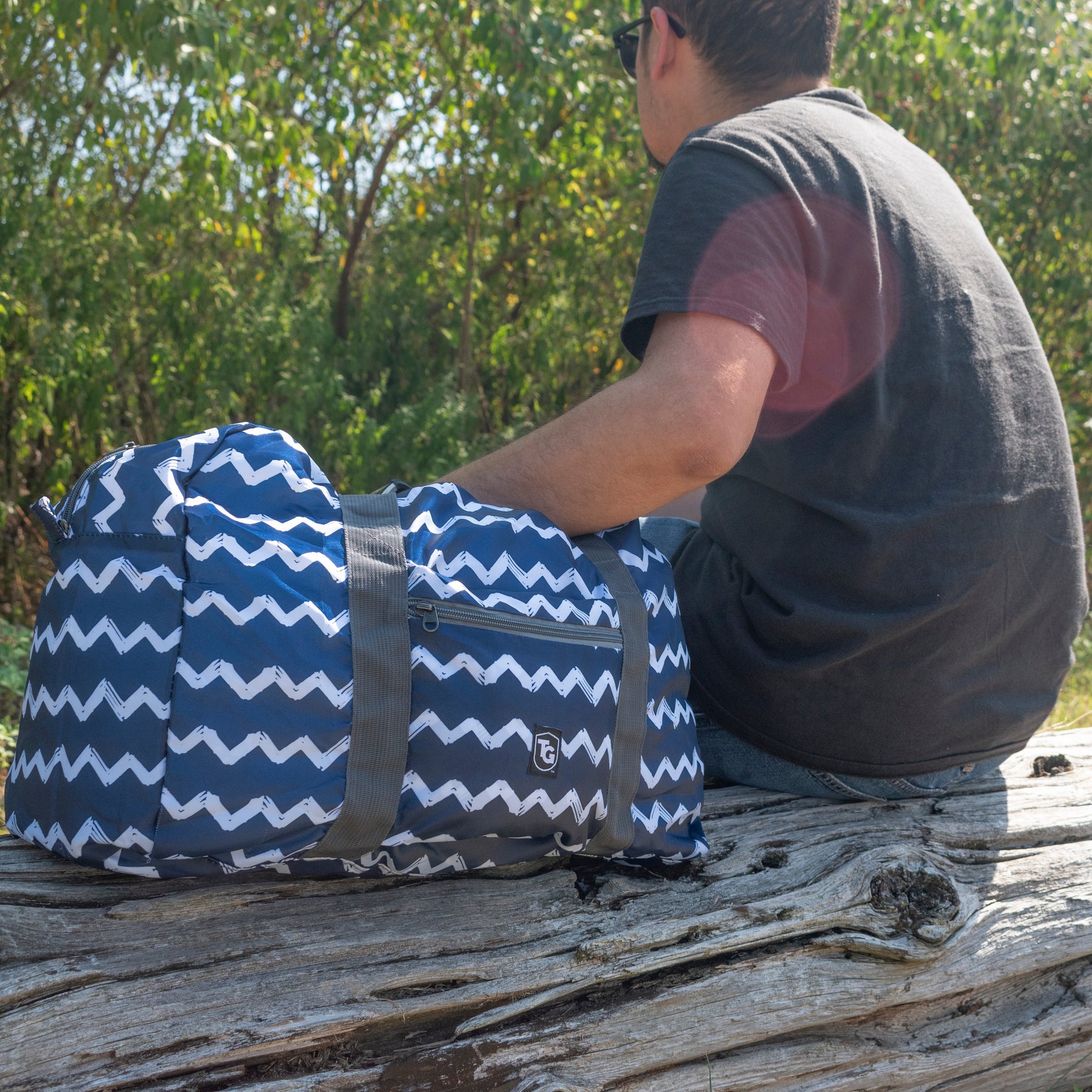Man sitting on a log with the TrailGear 30 Liter Duffel Bag next to him.