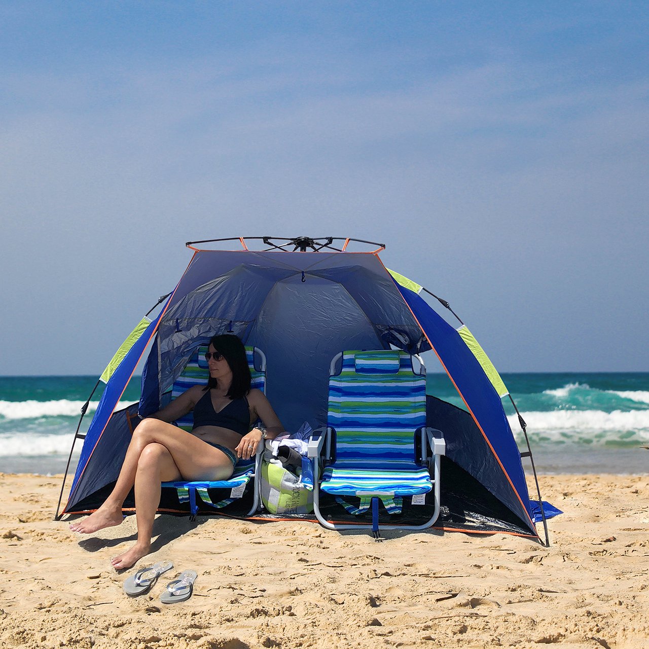 Woman relaxing on the beach under the Bliss Hammocks Pop-Up Beach Tent. She is sitting in one of our Bliss Beach Chairs - Beach