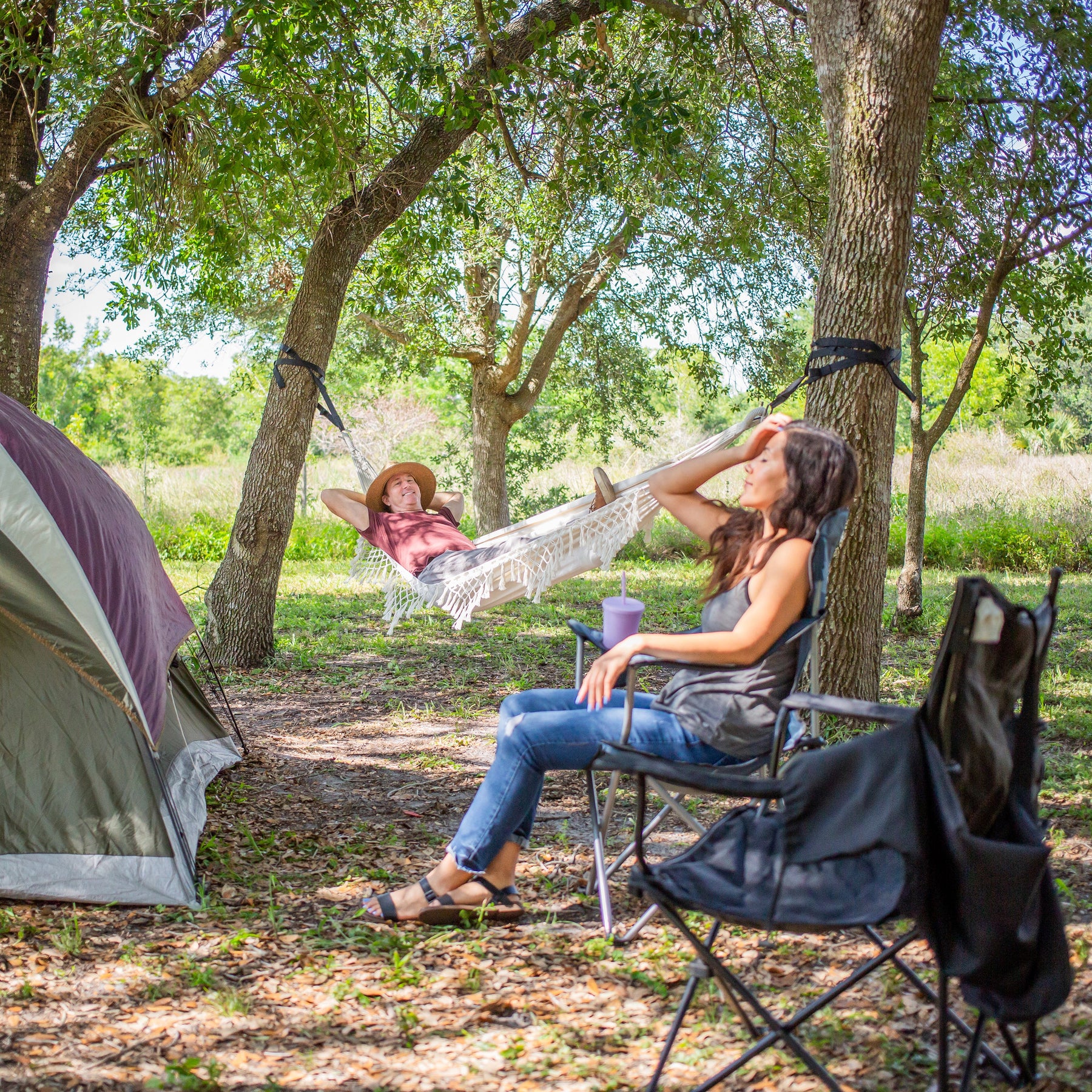 Woman relaxing in the Bliss Hammocks 40" Wide Hammock in a Bag with Fringe hung between two trees in a camp site.