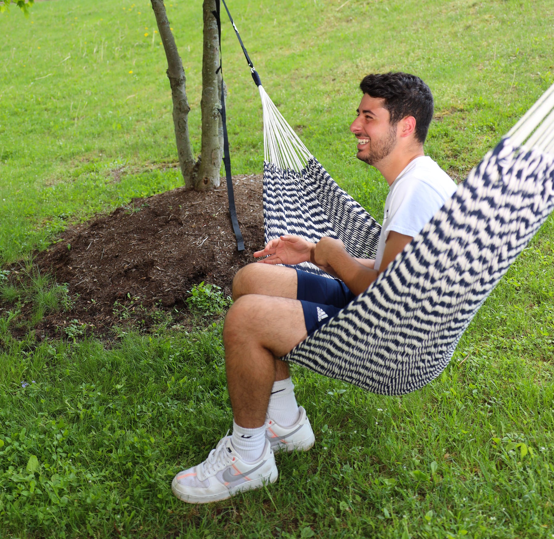 Man sitting in a Bliss Hammocks 39-inch Brazilian Style Rope Hammock with Braided Rope Ends with a zebra-like pattern tied to a tree outside.