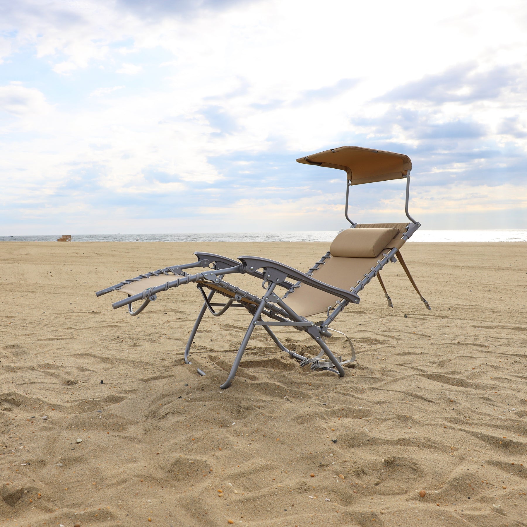 Taupe beach recliner with a canopy reclined on the sand.