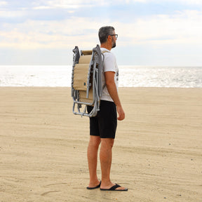Man carrying the taupe beach recliner on the beach using the back straps.