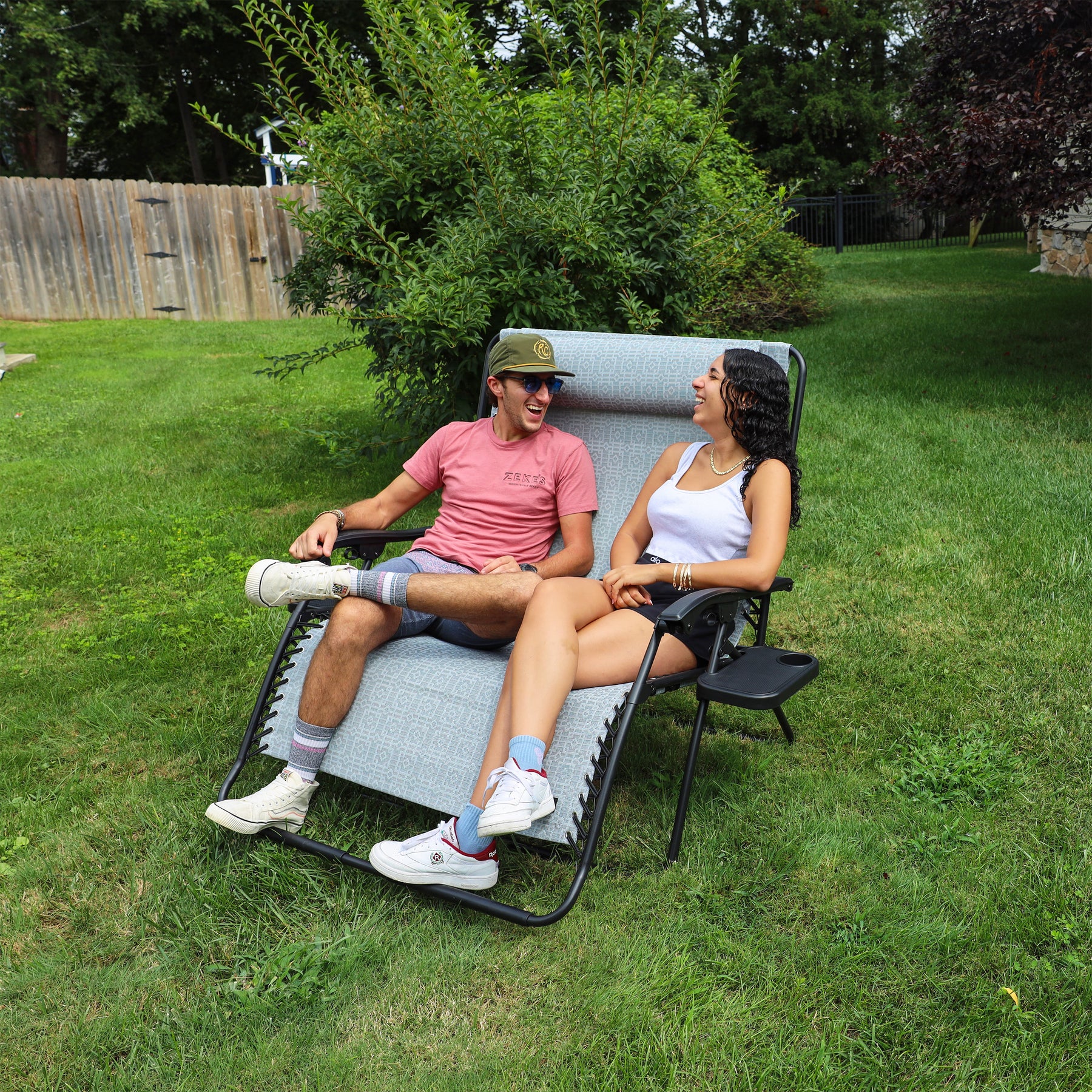Boy and Girl sitting and laughing outside in a Bliss Hammocks 45-inch Wide 2-Person Zero Gravity Chair with Pillow and Drink Tray in the gray variation.