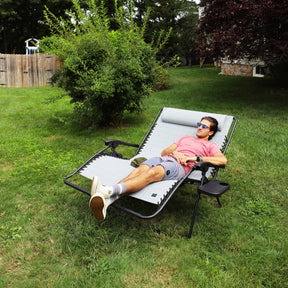 Man relaxing outside in the grass on a Bliss Hammocks 45-inch Wide 2-Person Zero Gravity Chair with Pillow and Drink Tray in the gray variation.