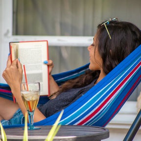 Woman reading a book in a Bliss Hammocks 40-inch Wide Hammock with a drink on the table beside her.