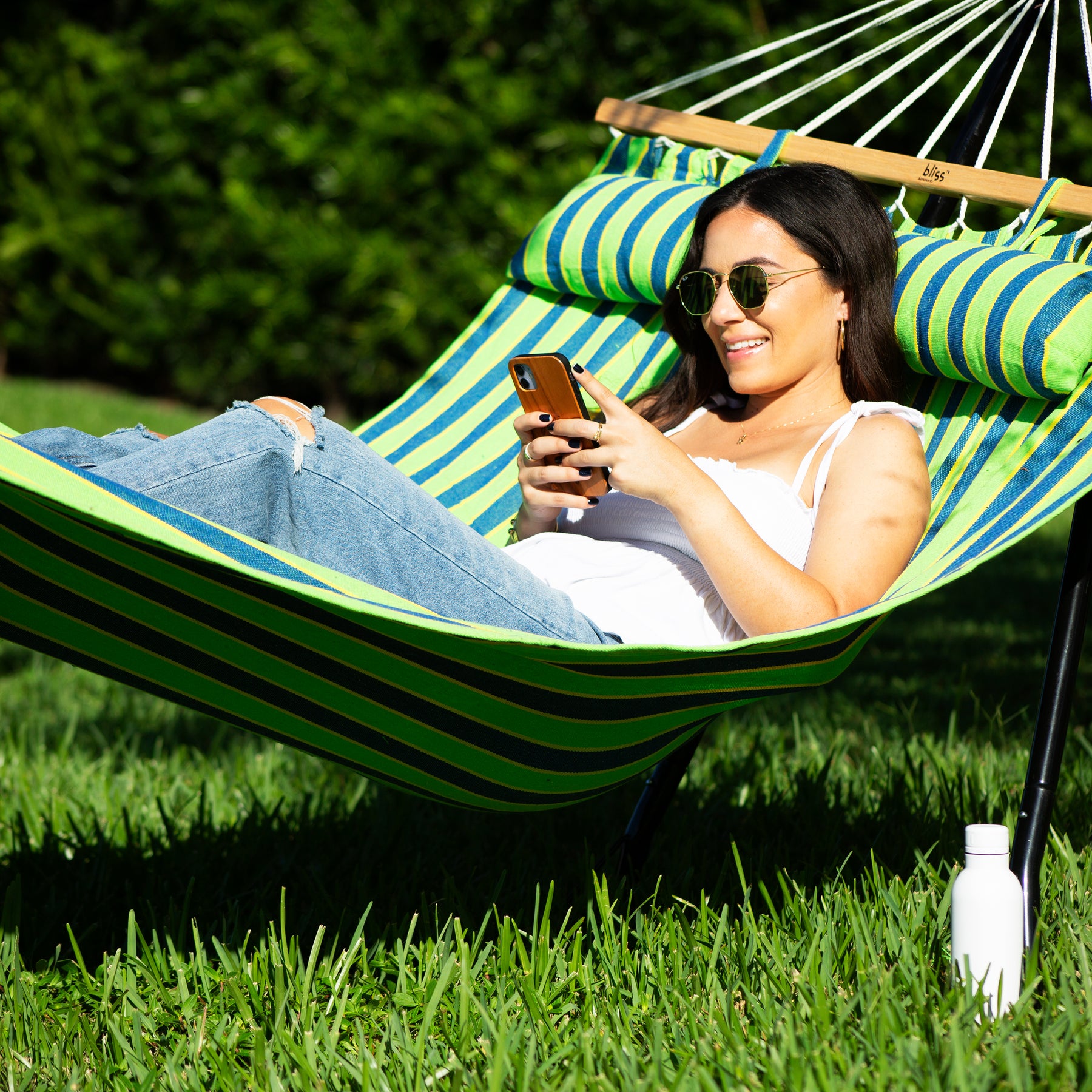 Woman wearing sunglasses is using her phone while relaxing on a sunny day outside in a Bliss Hammocks 48-inch Wide Caribbean Hammock.