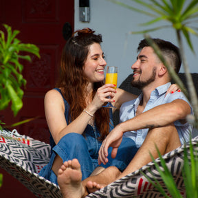 Man and woman sitting in a Bliss Hammocks 55-inch Wide 2-Person Reversible Quilted Hammock. They are smiling at each other and the woman is holding a drink in her hand.
