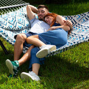 Man and woman laying in a Bliss Hammocks 55-inch Wide 2-Person Reversible Quilted Hammock with their legs hanging off onto the grass.