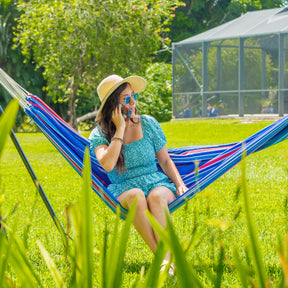 A woman on the phone while sitting in a Bliss Hammocks hammock outside in the grass.