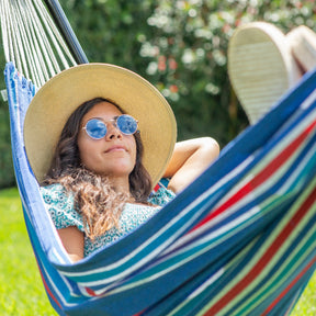 A woman relaxing in a Bliss Hammocks hammock outside with a sunhat and sungalsses.