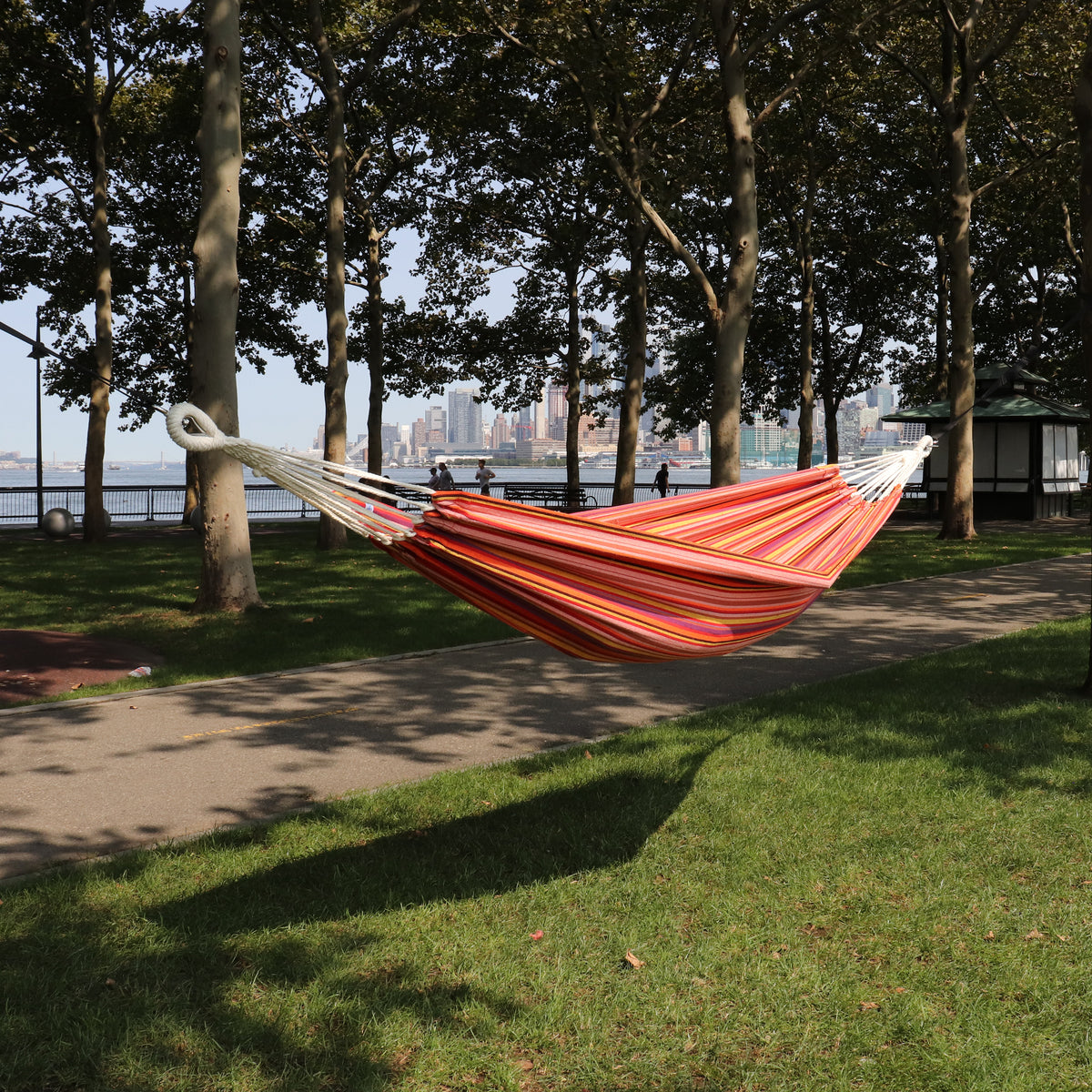 Bliss Hammocks 40-inch Wide Hammock in a Bag with Hand-woven Rope loops in the toasted almond variation hanging between two trees in a park.