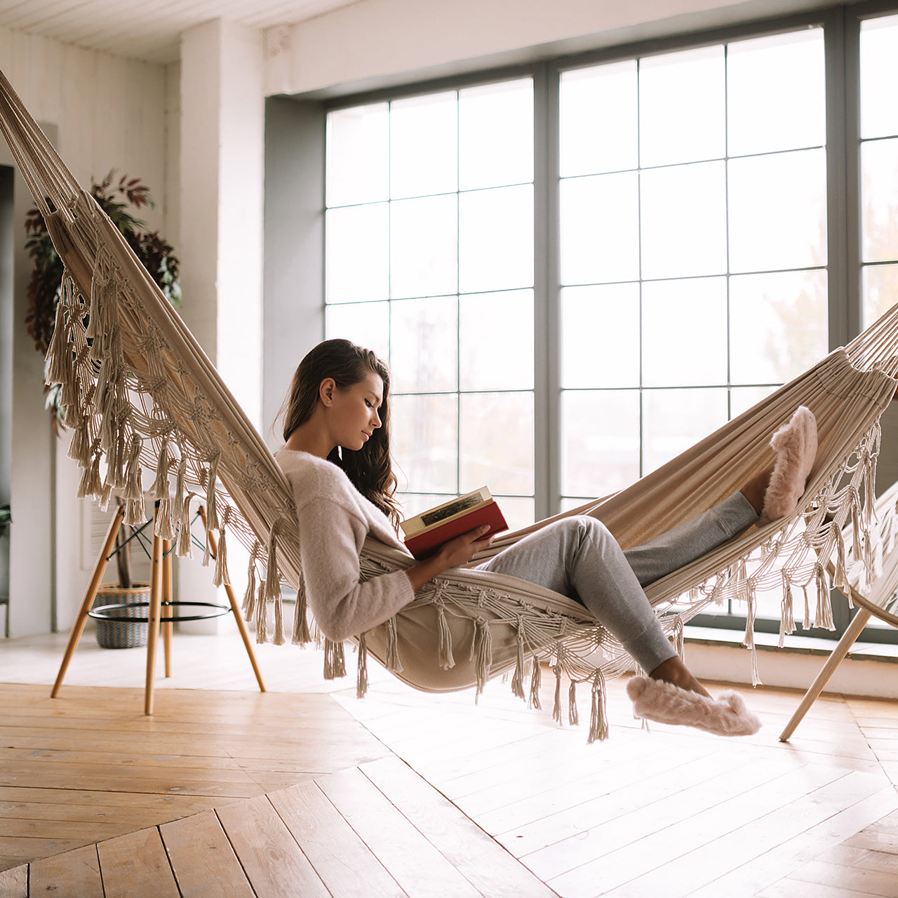 Women reading a book in the Bliss Hammocks 40-inch Wide Hammock in a Bag with Fringe hanging in a room.