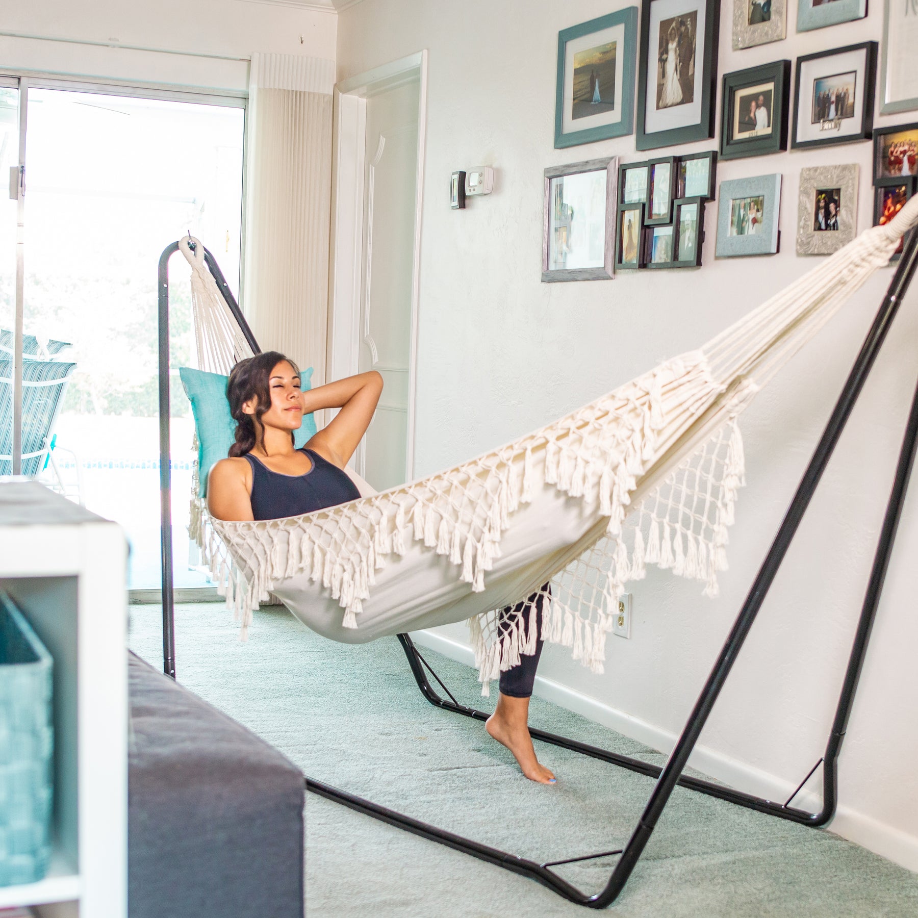 Woman relaxing a Bliss Hammocks fringed hammock attached to a hammock stand inside a house.