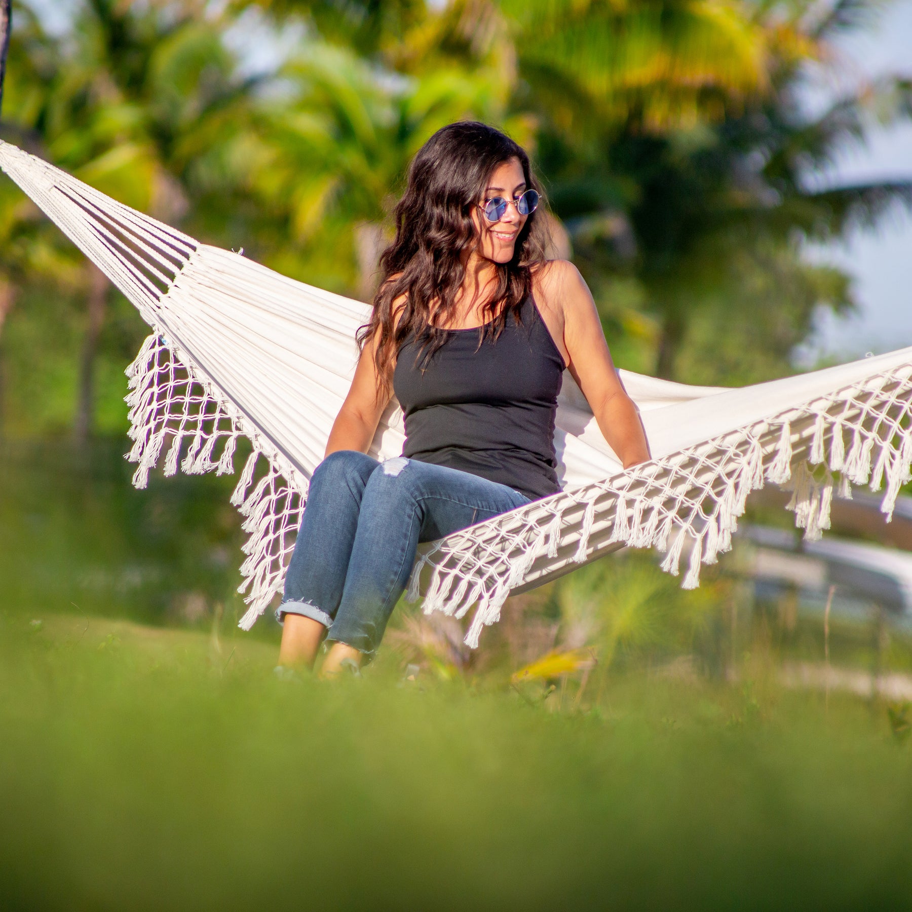 Woman with sunglasses sitting on the Bliss Hammocks 40-inch Wide Hammock in a Bag with Fringe.