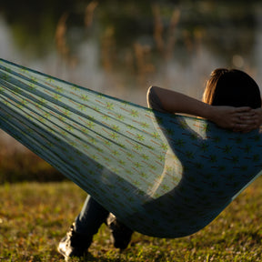Person relaxing outside, leaning back in the Bliss Hammocks 55-inch Mesh Hammock with a palm tree pattern.