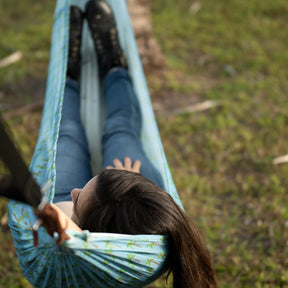 Top-view of a girl laying in the Bliss Hammocks 55-inch Mesh Hammock with a palm tree pattern, looking down from the tree strap.