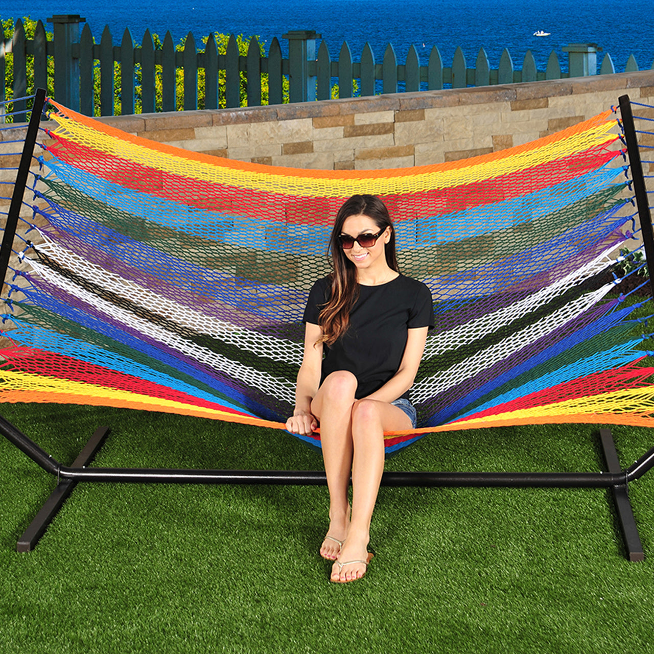 Woman sitting on the Bliss Hammocks 60-inch Wide Multi-Color Rope Hammock with Spreader Bars.