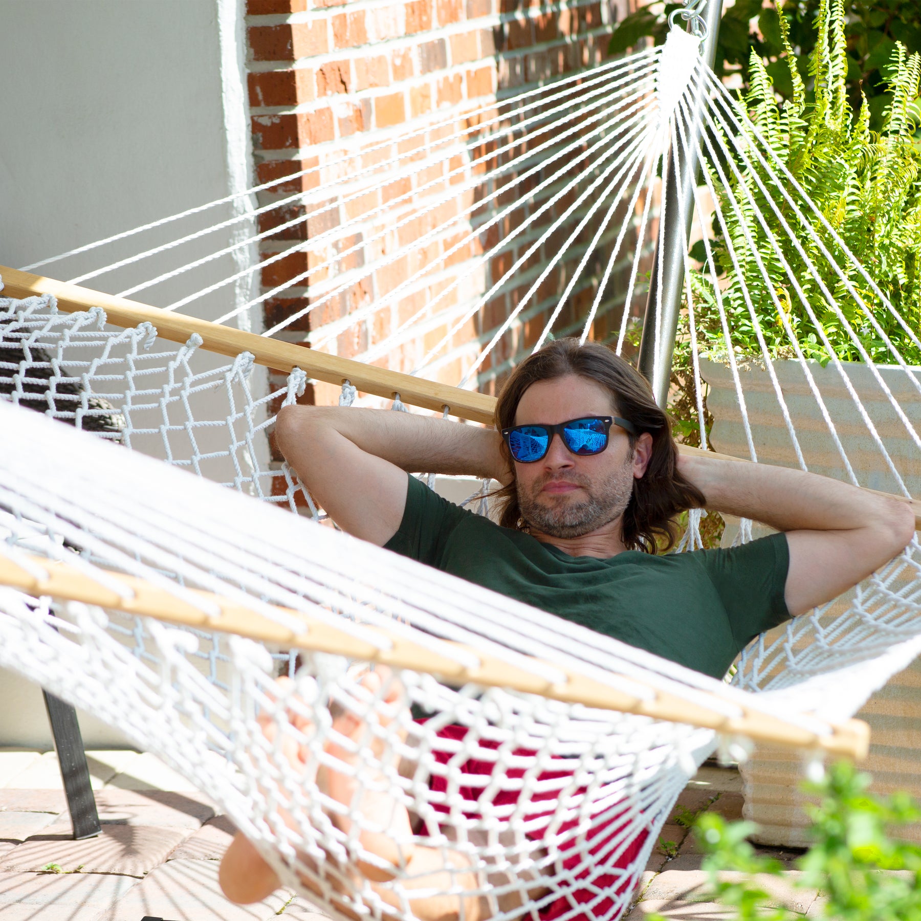 Man wearing sunglasses relaxing outside in a Bliss Hammocks 60-inch Wide Polyester Rope Hammock.