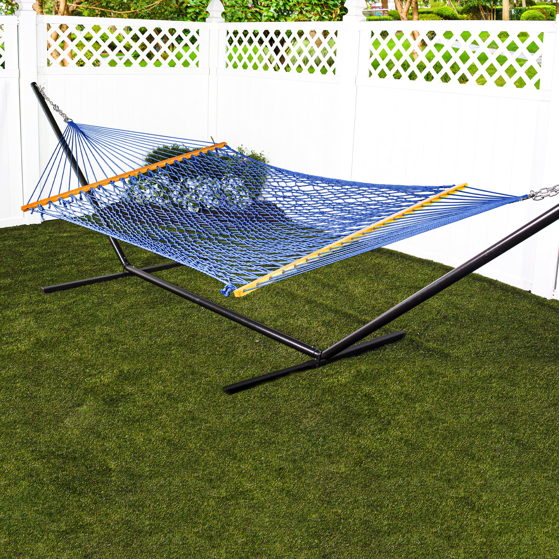 Blue variation of Bliss Hammocks 60-inch Wide Cotton Rope Hammock with a stand outside in the lawn near a fence.