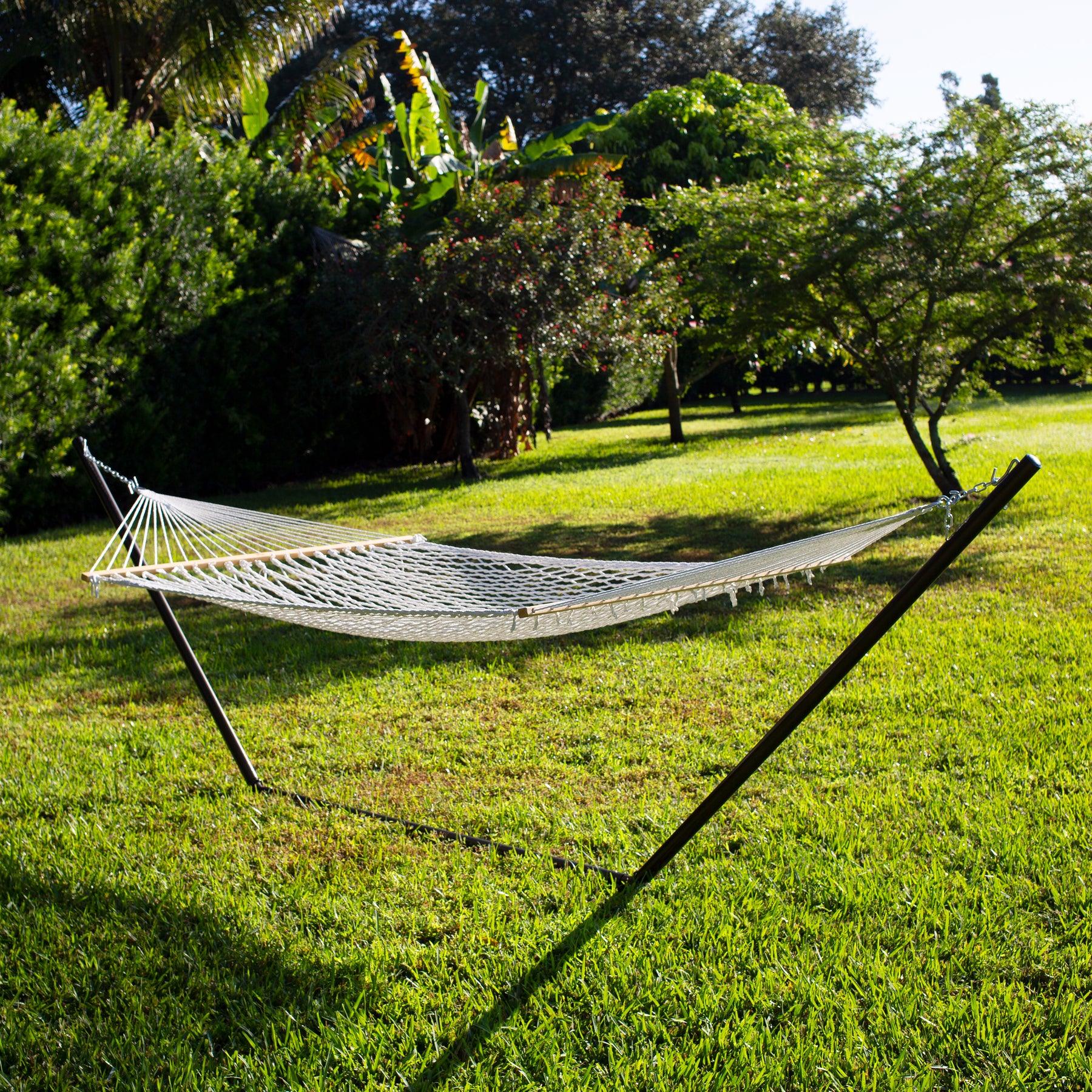 White variation of Bliss Hammocks 60-inch Wide Cotton Rope Hammock hooked up to a stand outside in the grass.
