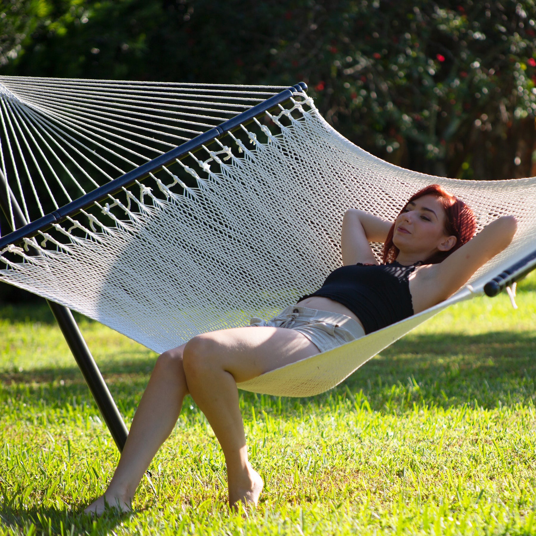 Woman laying back onto the Bliss Hammocks 55-inch Wide 2-Person Weekender Deluxe Hammock with Spreader Bars while her feet touch the grass.