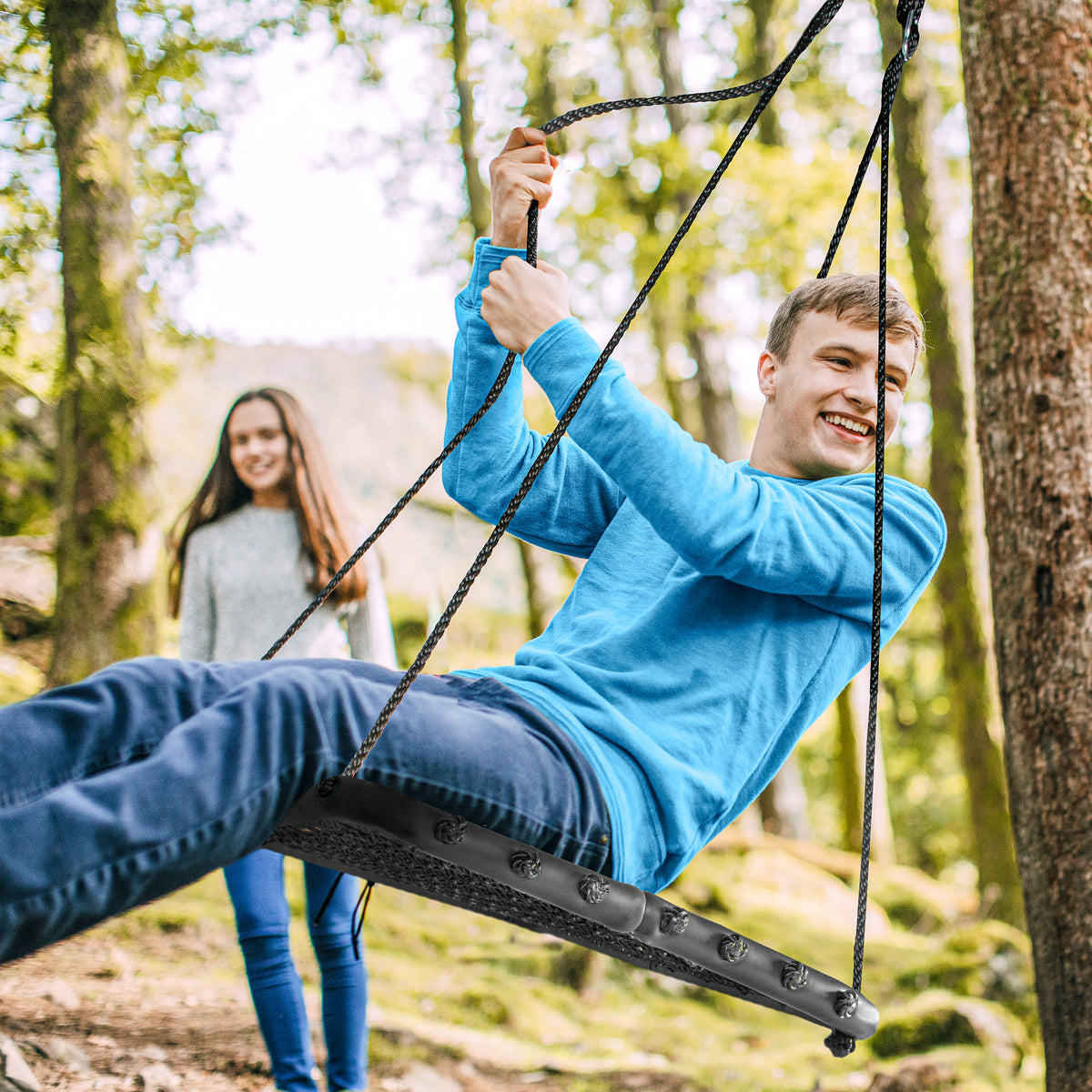 Boy swinging from a tree on the Bliss Outdoors Rectangular Tree Glider with Foam Frame. A girl watches him have fun in the background.