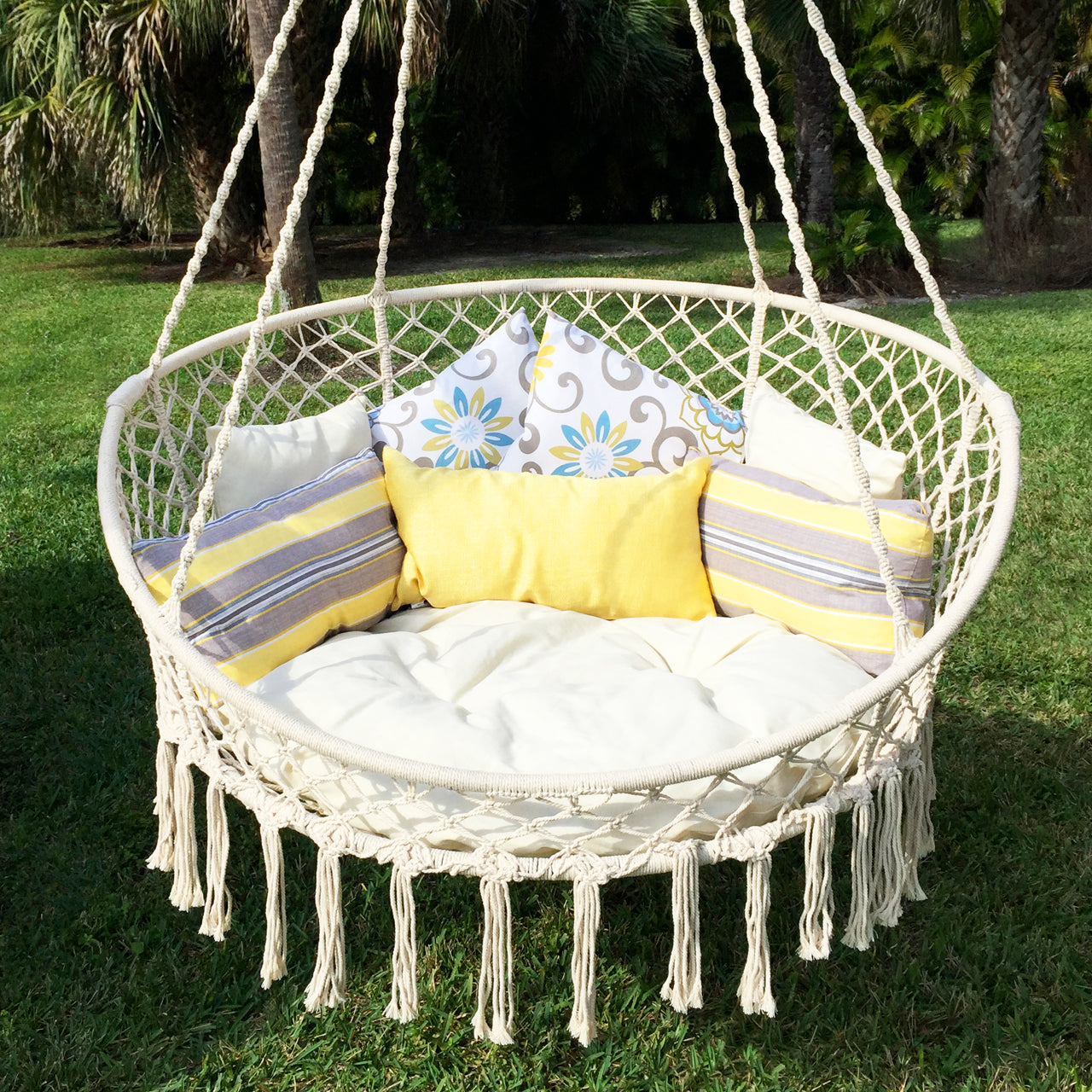 Bliss Hammocks 55-inch 2 Person Bohemian Style Macramé Swing Chair with Pillows hanging outside above the grass.