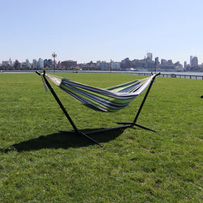 Bliss Hammocks 60-inch Wide Hammock & Built-in Stand in the Garden Stripe variation in the grass on a sunny day with a section of New York City in the background.