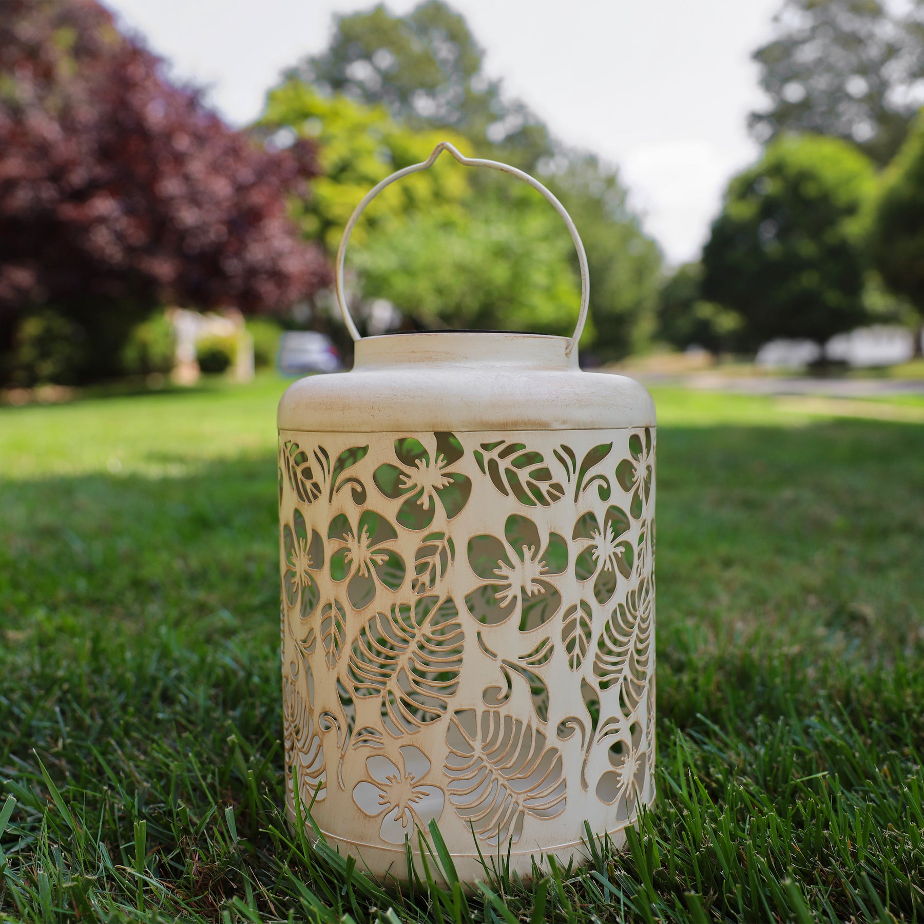 Antique White Solar Lantern with tropical flower design standing on grass.