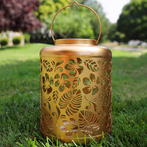 Gold Solar Lantern with tropical flower design standing on grass.