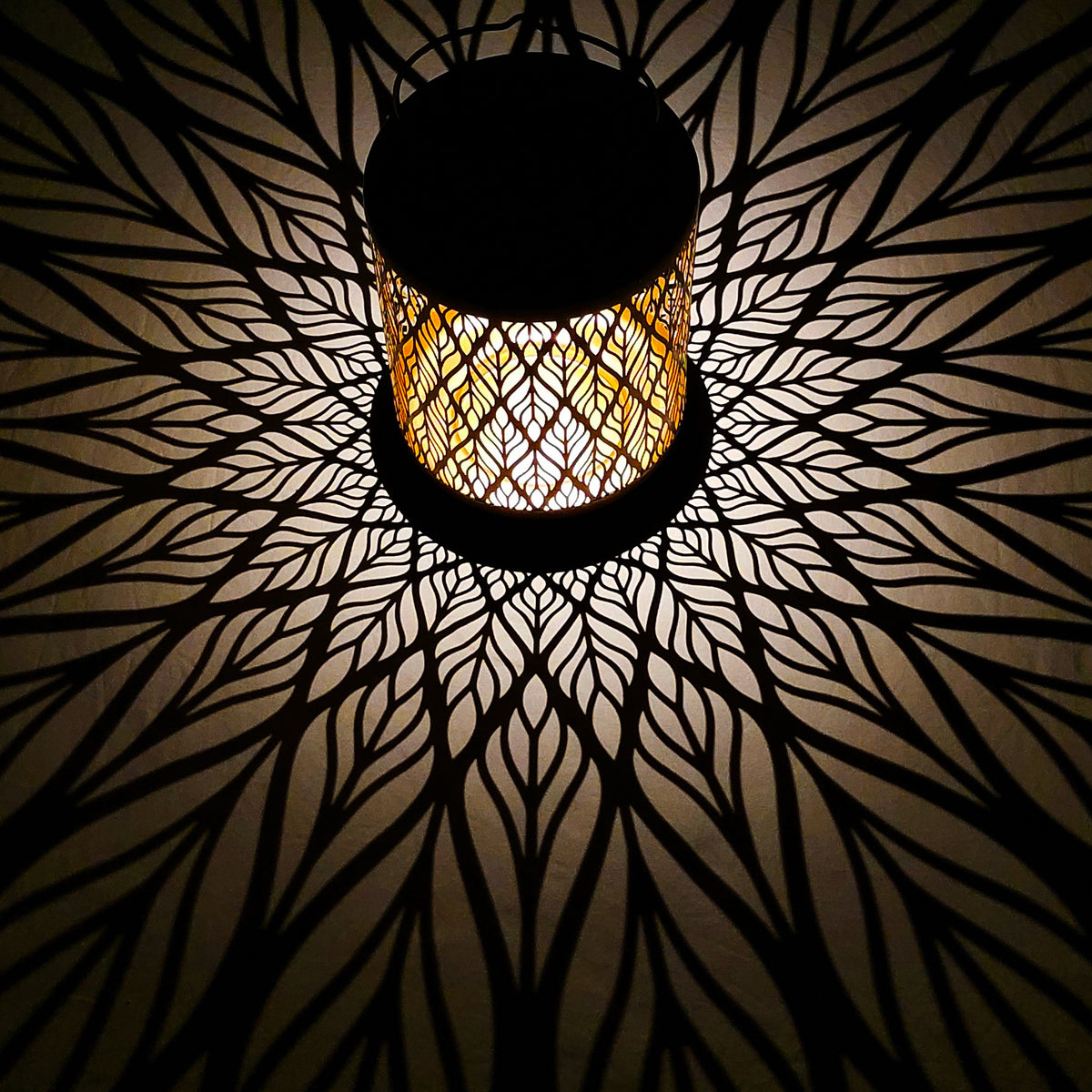 Bliss Outdoors 12-inch Tall Hanging and Tabletop Decorative Solar LED Lantern with Unique Diamond Leaf Design turned on and creating a cool pattern of light on the surface around it.