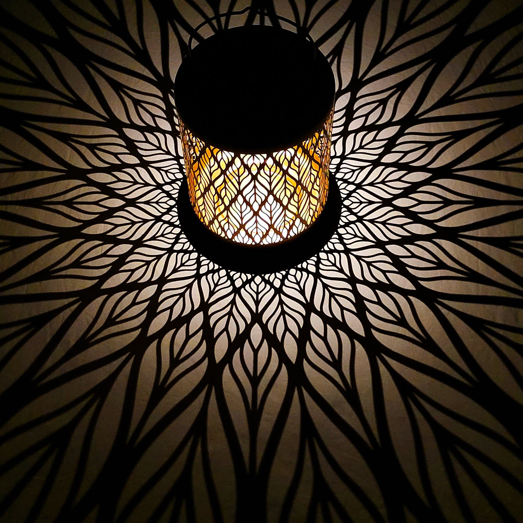 Bliss Outdoors 12-inch Tall Hanging and Tabletop Decorative Solar LED Lantern with Unique Diamond Leaf Design turned on and creating a cool pattern of light on the surface around it.