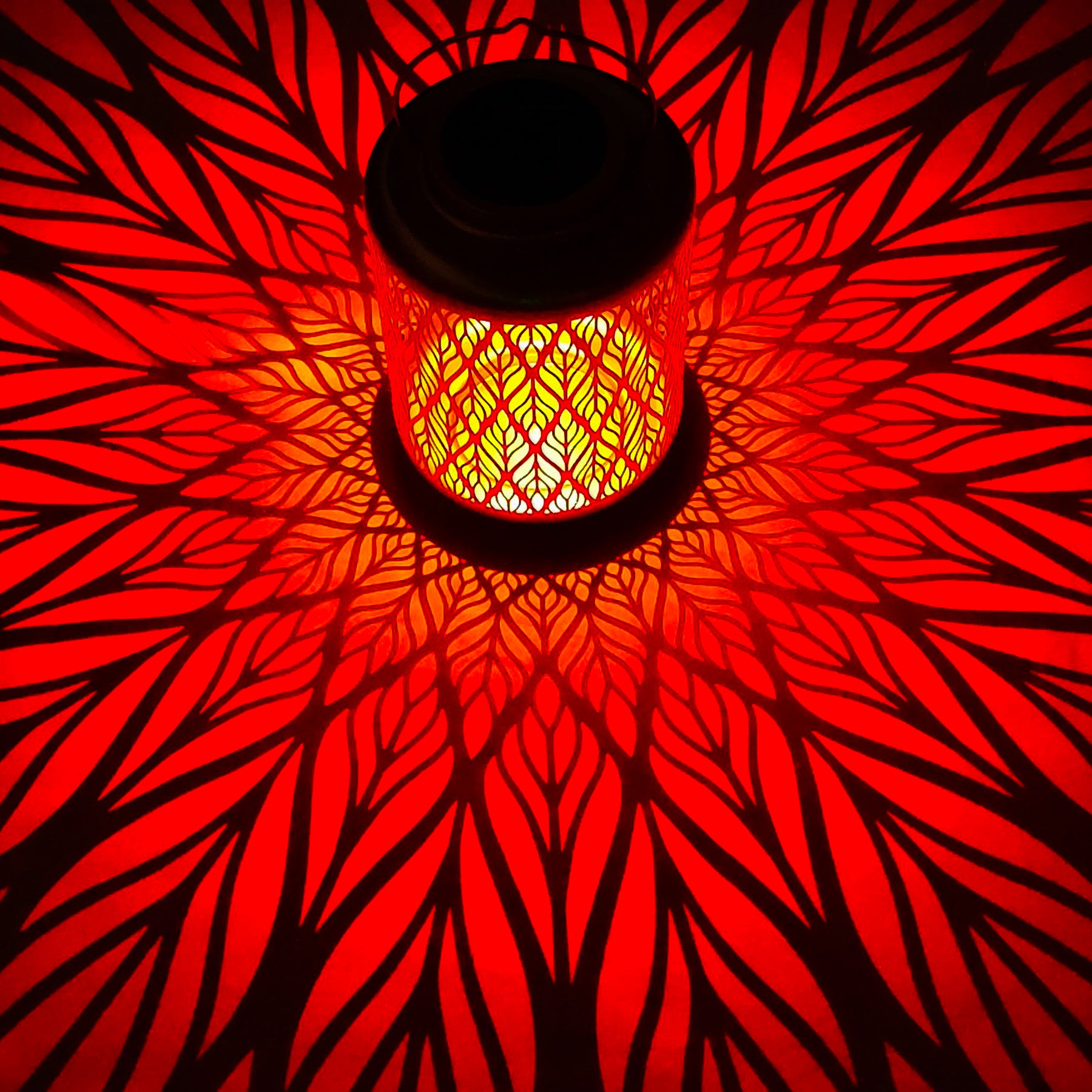 Bliss Outdoors 12-inch Tall Hanging and Tabletop Decorative Solar LED Lantern with Unique Diamond Leaf Design turned on and creating a cool pattern of red light on the surface around it.