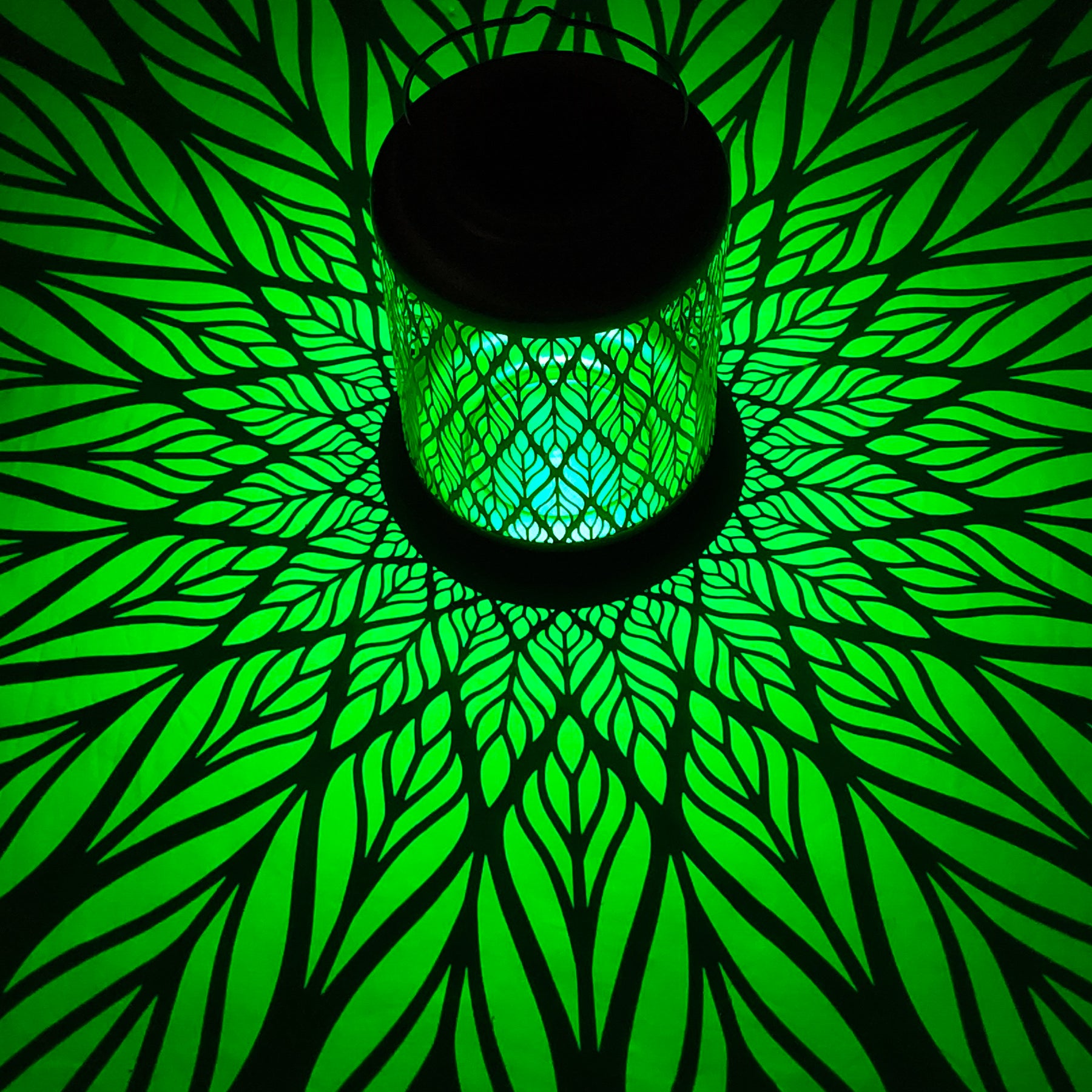 Bliss Outdoors 12-inch Tall Hanging and Tabletop Decorative Solar LED Lantern with Unique Diamond Leaf Design turned on and creating a cool pattern of green light on the surface around it.