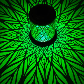 Bliss Outdoors 12-inch Tall Hanging and Tabletop Decorative Solar LED Lantern with Unique Diamond Leaf Design turned on and creating a cool pattern of green light on the surface around it.