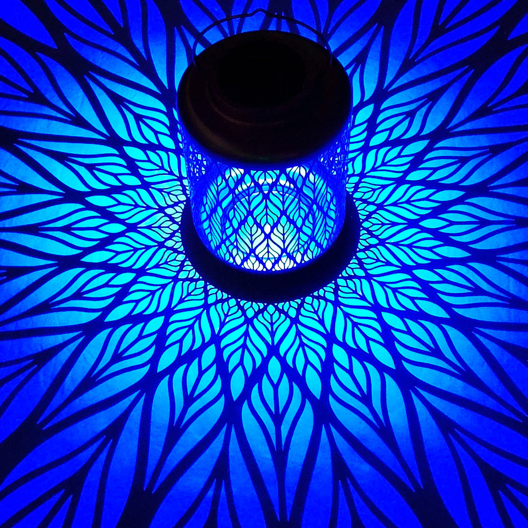 Bliss Outdoors 12-inch Tall Hanging and Tabletop Decorative Solar LED Lantern with Unique Diamond Leaf Design turned on and creating a cool pattern of blue light on the surface around it.
