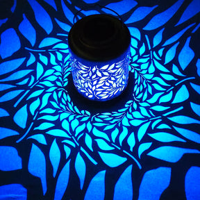 Bliss Outdoors 12-inch Tall Hanging and Tabletop Decorative Solar LED Lantern with Unique Olive Leaf Design turned on and creating a cool pattern of blue light on the surface around it.