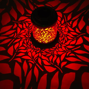 Bliss Outdoors 12-inch Tall Hanging and Tabletop Decorative Solar LED Lantern with Unique Olive Leaf Design turned on and creating a cool pattern of red light on the surface around it.