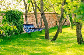 Bliss Hammocks 55-inch Wide Ventaleen Breathable Performance 2 Person Hammock with Pillow with blue and white stripes hanging outside between two trees.