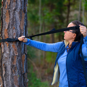 Woman securing a tree strap onto a tree outside.