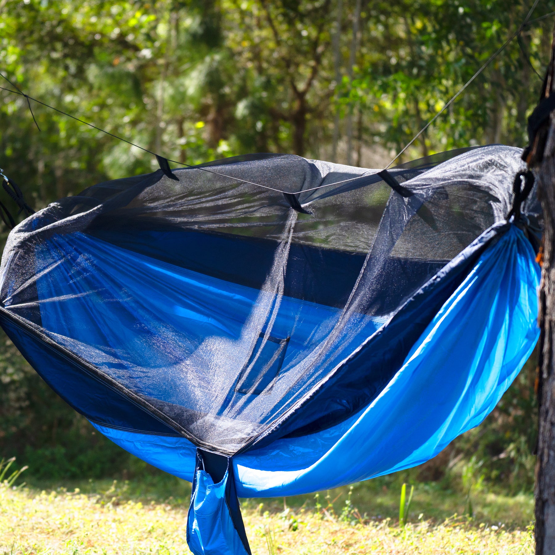 Bliss Hammocks 54-inch Wide Hammock in a Bag with mosquito net and tree straps hung outside between two trees.